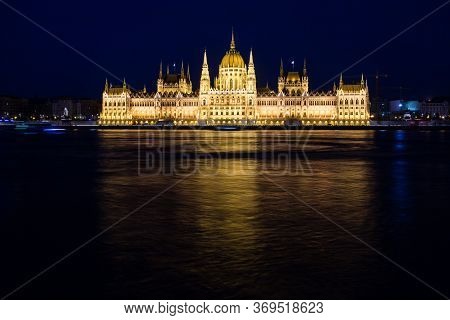 Illuminated Budapest Parliament Building At Night With Dark Sky And Reflection In Danube River, Hung
