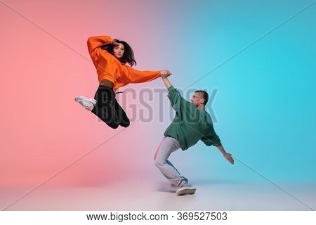 In Jump. Boy And Girl Dancing Hip-hop In Stylish Clothes On Colorful Gradient Background At Dance Ha
