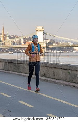 Budapest, Hungary - Feb 9, 2020: Female Jogger By Danube River In The Afternoon With Liberty Bridge 