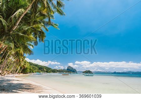 Palm Trees Of Corong Corong Beach With Traditional Boats And Blue Sky In El Nido, Palawan Island, Ph