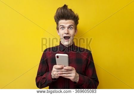 Shocked Guy With Funny Hairstyle Use Smartphone On Yellow Isolated Background, Hipster Holds Phone A