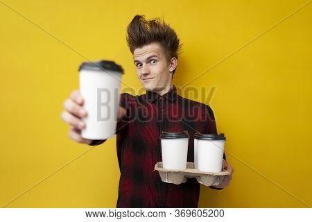 Guy With A Funny Hairstyle Suggests Drinking Coffee On A Yellow Isolated Background, Hipster Gives C