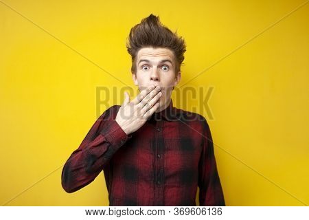 Shocked Guy Closes His Mouth With His Hands On A Yellow Isolated Background, Scared Man Is Surprised