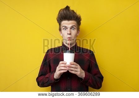 Shocked Guy Drinks Energy Coffee On A Yellow Isolated Background, A Man With A Funny Hairstyle Holds