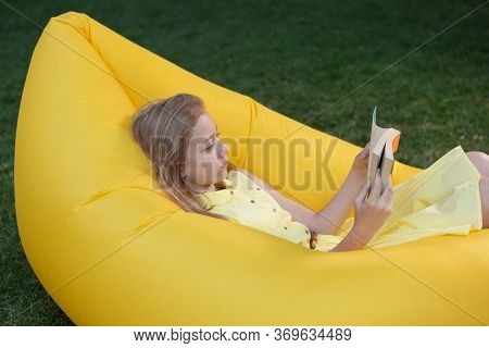 Girl Lying On An Air Sofa And Reading A Book, Resting In Nature
