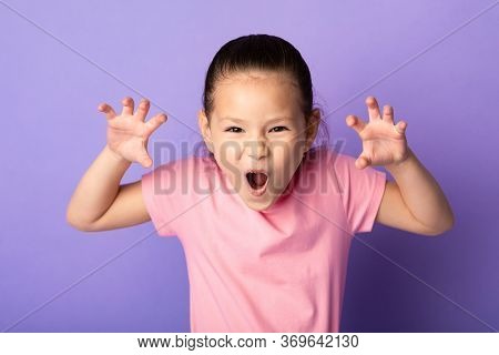 Having Fun. Playful Little Asian Girl Imitating Tiger, Roaring And Grimacing Over Pastel Purple Stud