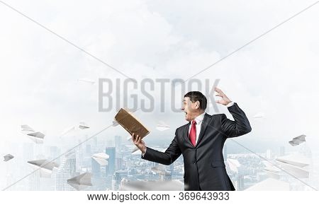 Expressive Businessman Holding Open Book. Emotional Man In Suit And Tie Standing On Downtown Backgro