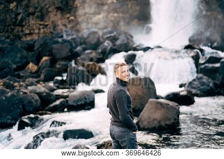 A Guy In A Black Knitted Sweater Stands On Rocks Near Ehsaraurfoss Falls, Ehsarau River, National Pa