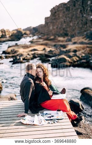 A Guy Hugs A Girl Artist Who Paints A Picture In The Album With Watercolors. Near Ehsaraurfoss Water