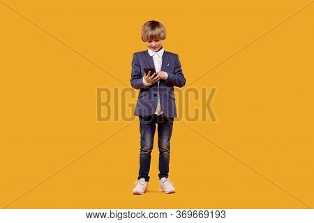 Cheerful Boy In A White Shirt In Full Growth Plays In The Phone In His Hands.