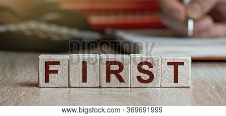 Word First Made With Cube Wooden Block On A Desk.