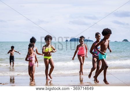 African American, Kids Group In Swimwear Enjoying Running To Play The Waves On Beach. Ethnically Div