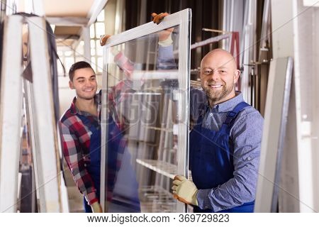 Portrait Of Happy Smiling Workers In Coverall Working With Pvc Window At Factory