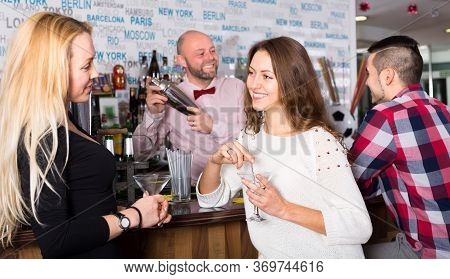 Two Women And A Man At The Bar. Women Are Talking And A Man Is Waiting For His Drink While The Barte
