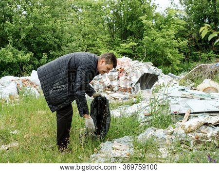 A Middle-aged Man In Black Clothes Puts Grbage In A Black Bag