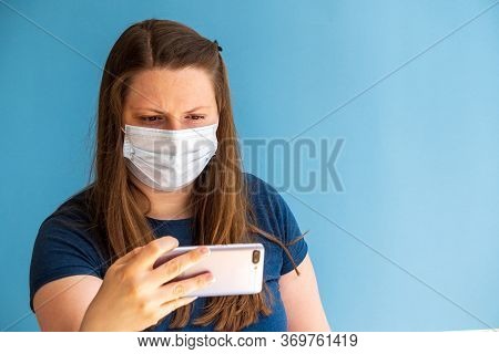 European Girl Blogger In Medical Mask On The Blue Background With Mobile Phone In Your Hand. Phone W