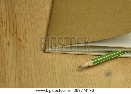 Green Pencil And Brown Notebook On Wooden Desk