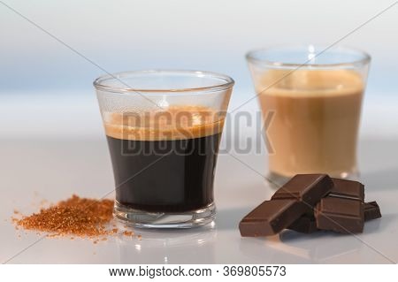 An Espresso Coffee Surrounded By Brown Sugar, Chocolate Squares And An Out Of Focus Cortado At The B