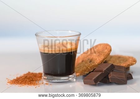 View Of An Espresso Coffee Surrounded By Chocolate Squares, Cookies And Brown Sugar On A Glass Table