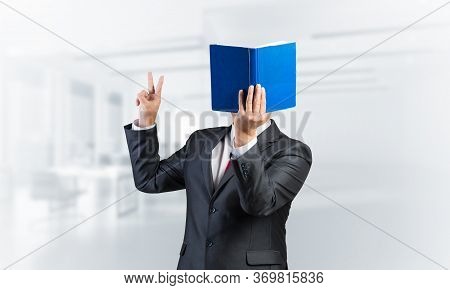 Businessman Covered His Face With Book And Finger Pointing Up. Portrait Of Man In Business Suit Stan