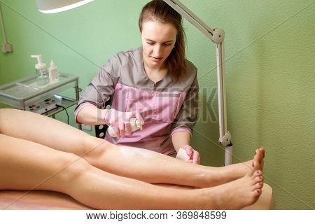 Cosmetologist Applying Anesthetic To Womans Leg Before Hair Removal Procedure.