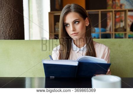 Beautiful Girl At A Table In A Cafe With A Notebook.