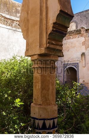 Detail Of A Decorative Column In A Yard Of An Abandoned House. Wild Growing Bushes. Gate With Tradit