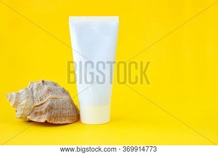 White Cosmetic Tube Container And Seashell On A Yellow Background. The Concept Of Skin Care In A Bea