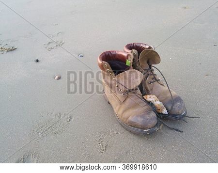Seashells And Pair Of Worn Boots Lying On The Sand On The North Sea Coast