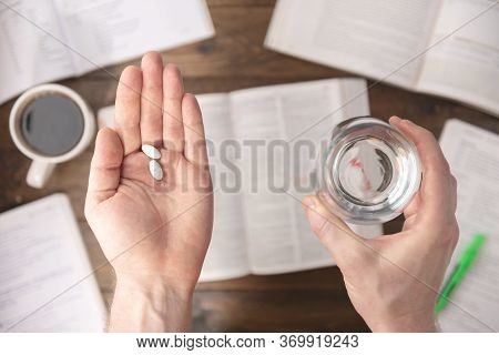 Work Stress Concept. Hands Holding Pills And Glass Of Water Above Workspace Desk With Pharmaceutical
