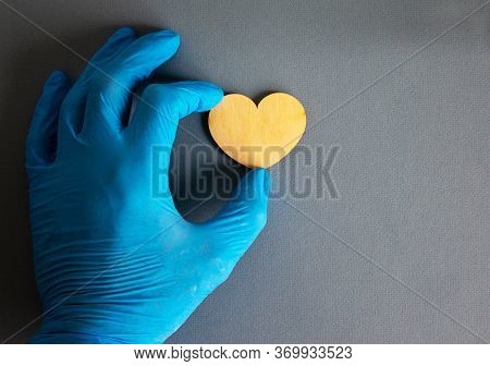 Wooden Heart, Hand In Blue Glove On Blue Background.