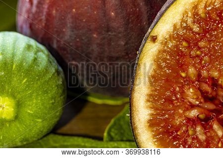 Close Up Of Figs On Top Of Green Leaves On Rustic Wooden Background