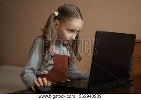 Serious Little Girl Is Concentrated In Front Of Her Black Laptop While Focused On Doing Homework Dur