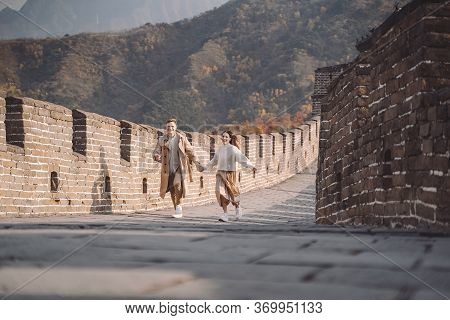 Beautiful Young Couple Running And Jumping At The Great Wall Of China.