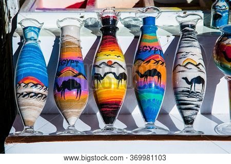 Hurghada, Egypt- Jan 27 , 2020:Decorative glass bottles with colored sand inside and shapes of desert and camels in street shop. Egupt.