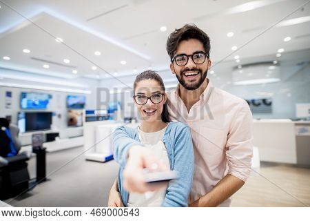 Couple Standing In Tech Store. In Girl's Hand Remote Control For Plasma Tv. New Technologies Concept