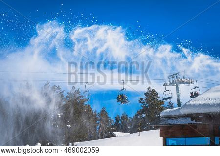 Snow Cannon Spreading Fresh Snow Powder On A Ski Slope. Skiers Riding Up On Chair Lift. Winter Ski H