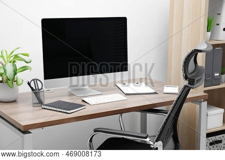 Cozy Workspace With Computer On Desk, Chair And Bookcase Near White Wall At Home