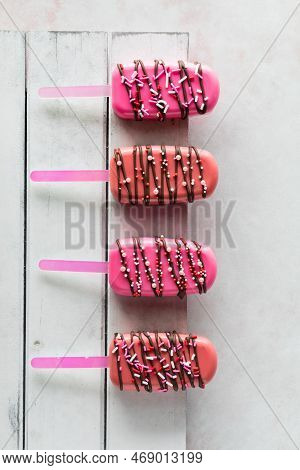 A Row Of Decorated Cakesicles For Valentines Day, On A White Wooden Board.