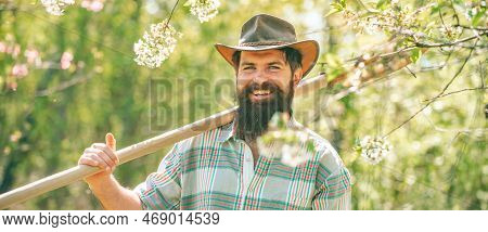 Man Working In Garden Near Flowers Garden. Gardener Work In Yard With Garden Tools And Have Good Tim