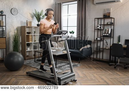 Pozitive African Woman In Sports Clothes And Sneakers Listening Music In Headphones While Using Smar
