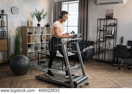 Pozitive African Woman In Sports Clothes And Sneakers Listening Music In Headphones While Using Smar