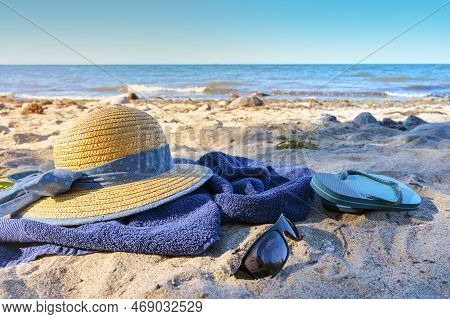 Straw Hat And Flip Flops On A Blue Towel On The Natural Beach On The Sea, Tourist Resort On The Balt