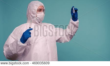 A Male Doctor In Protective Overalls And A Mask Holds An Ampoule With A Vaccine And Syringe In His H