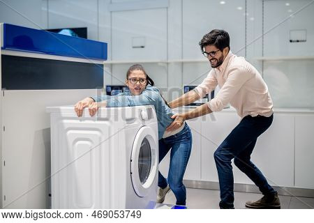 Man Taking Away Wife From Washing Machine. Whiteware Department Interior.