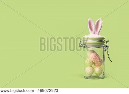Easter Bunny Ears Sweets Glass Jar With Tiny Eggs Inside On Spring Yellow Green Edgeless Background.