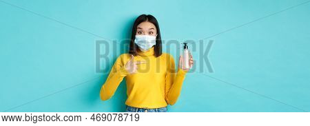 Covid-19, Social Distancing And Pandemic Concept. Enthusiastic Asian Woman In Face Mask Pointing Fin
