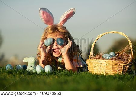 Cute Excited Bunny Child Boy With Rabbit Ears. Child With Easter Eggs In Basket Outdoor. Boy Laying 