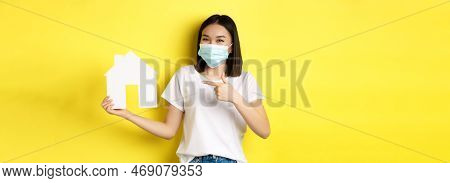 Covid-19, Pandemic And Real Estate Concept. Cheerful Asian Woman Smiling In Medical Mask, Showing Pa
