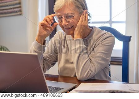 Smiling Mature Woman Sitting At Table With Laptop And Book Following Online Course. Attractive Senio